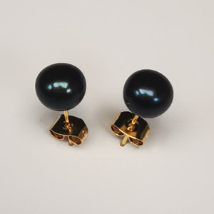 May include: A pair of black pearl stud earrings with gold posts.