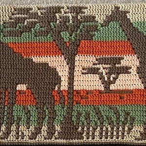 May include: Crocheted wall hanging featuring a repeating pattern of brown moose silhouettes against a background of green, brown, and beige stripes.