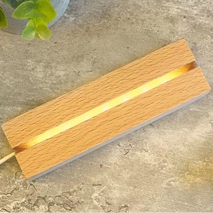 May include: A wooden light-up display stand with a warm white LED strip running down the centre. The stand is made of light wood and has a natural finish.