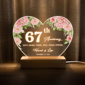 May include: A heart-shaped anniversary light with the text "67th Anniversary" and the names "Hannah & Leon." The design includes pink floral accents and the date "September 13, 2024."
