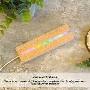 Pu&ograve; includere: Un portacandele in legno con una striscia di luci LED che cambiano colore. Le luci mostrano attualmente un arcobaleno di colori. Il portacandele &egrave; su una superficie grigia.