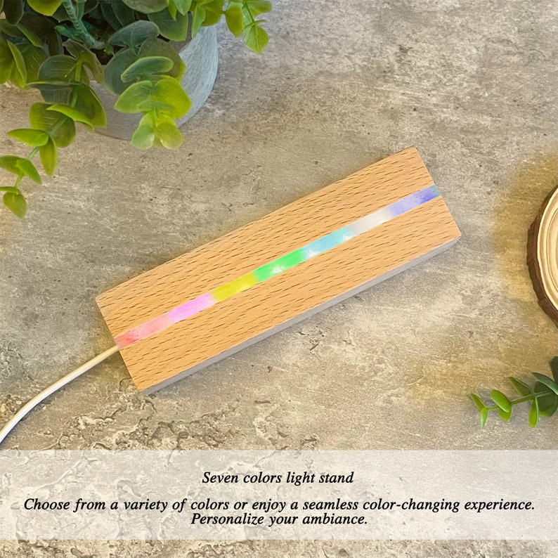 Pu&ograve; includere: Un portacandele in legno con una striscia di luci LED che cambiano colore. Le luci mostrano attualmente un arcobaleno di colori. Il portacandele &egrave; su una superficie grigia.