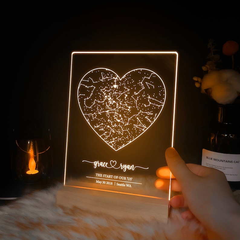 May include: A white LED light with a heart-shaped constellation design. The text "grace ryan" is written below the heart, along with the text "THE START OF OUR 'US'" and "May 30 2018 | Seattle WA".