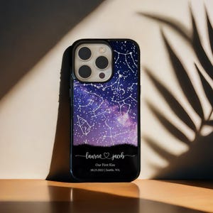 May include: A black phone case with a night sky design, showing constellations in white. The case is inscribed with the names "lauren & jacob" and the text "Our First Kiss 08.23.2022 | Seattle, WA" in a script font.