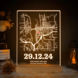 May include: A glowing map of a city, with a red heart indicating a spot. The date "29.12.24" and the text "THE NIGHT WE MET" are shown below. The base is made of wood, and the light has a warm tone.