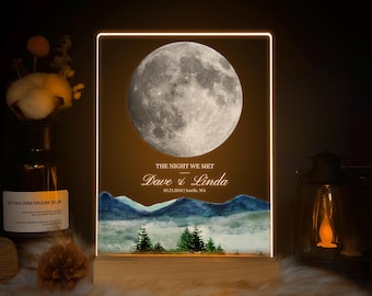 May include: Illuminated sign with a full moon graphic. The text reads "The Night We Met" with names "Dave & Linda" and a date. Below the text is a watercolor landscape of mountains and trees.