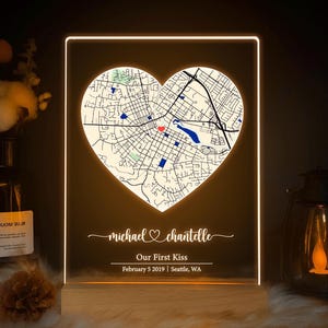 May include: An illuminated acrylic sign with a heart-shaped map of Seattle, WA. The map is lit with a warm light. Below the map, the names "michael & chantelle" are written, along with "Our First Kiss" and the date February 5, 2019.