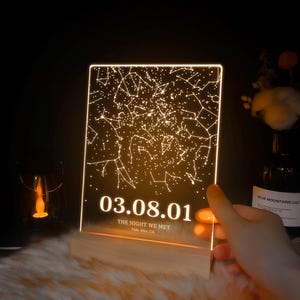 Puede incluir: Una luz de constelaci&oacute;n de cielo nocturno de acr&iacute;lico transparente con fondo blanco y la fecha 03.08.01, el texto "The Night We Met" y "Palo Alto, CA".