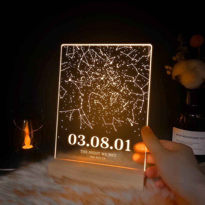 Puede incluir: Una luz de constelaci&oacute;n de cielo nocturno de acr&iacute;lico transparente con fondo blanco y la fecha 03.08.01, el texto "The Night We Met" y "Palo Alto, CA".