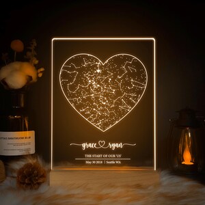 May include: A white LED night light with a constellation heart design. The heart is surrounded by the names "grace" and "ryan" with the text "The start of our 'us'" and the date "May 30 2018 | Seattle WA".