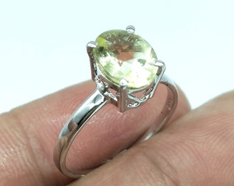 May include: A silver ring with a light yellow oval gemstone set in a delicate, ornate setting.