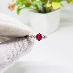 Peut inclure: Une bague en argent avec une pierre ovale rouge entourée de petites pierres blanches.