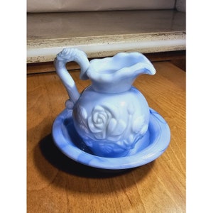 May include: A blue and white milk glass pitcher with a rose design. The pitcher is sitting on a matching blue and white saucer.