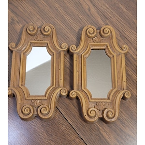May include: Two ornate wooden framed mirrors with a decorative scroll design. The mirrors are rectangular and have a beveled edge.