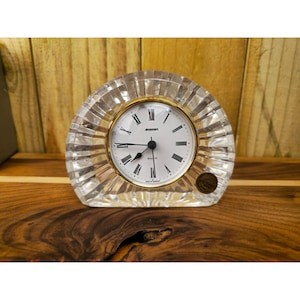 Puede incluir: Un reloj de cuarzo transparente con un bisel dorado y números romanos. La esfera del reloj es blanca con manecillas negras y la marca "Stanger". El reloj está encerrado en un material acanalado similar al cristal.