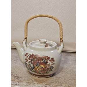 May include: White ceramic teapot with a woven bamboo handle. The teapot features a floral design with a pheasant and a red, brown, and gold color scheme.