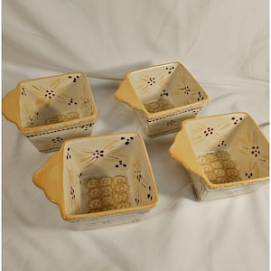 Könnte beinhalten: Set aus vier quadratischen Keramikschalen mit Griffen. Die Schalen sind mit einem floralen Muster in Braun- und Gelbtönen auf cremefarbenem Hintergrund verziert.