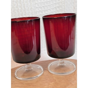 Può includere: Due bicchieri da vino in vetro rosso con steli e basi trasparenti. I bicchieri sono su una superficie di legno.