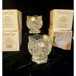 Puede incluir: Candelabros de cristal transparente con un patrón de diamantes y un borde festoneado. Los candelabros están etiquetados como "CAROLYN" y se muestran con sus cajas originales. Las cajas están etiquetadas como "MANHATTAN CANDLE LIGHTS".