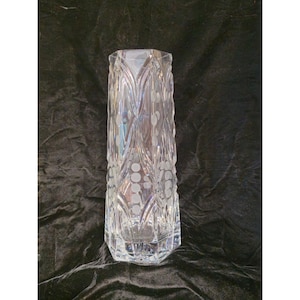May include: A clear glass vase with a hexagonal base and a tapered body. The exterior features a repeating pattern of vertical etched lines and frosted circular dots arranged in columns, creating a textured surface across the transparent glass.