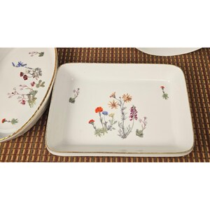 May include: A rectangular white porcelain serving dish with a gold-trimmed rim. The center features a detailed botanical illustration of various wildflowers in shades of orange, blue, yellow, and purple, with additional small floral sprigs.