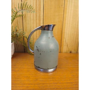 May include: A vintage light blue thermos with a silver handle and rim. The thermos has a ribbed design and shows signs of wear. A classic piece of kitchenware, ideal for serving hot or cold drinks.