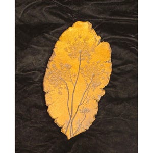 May include: A handcrafted, leaf-shaped decorative piece with a textured, golden-yellow surface. The design features an etched botanical pattern of delicate stems and flower heads, adding a natural, artistic touch to home decor.