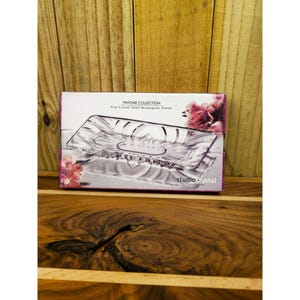 May include: A rectangular crystal platter in its original box. The box is white with the words "PAVONE COLLECTION" and "Fine Crystal Small Rectangular Platter". The platter is clear and has a decorative design. The brand name "studio crystal" is printed on the box.