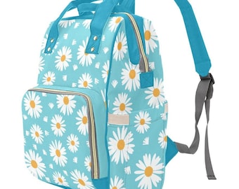 May include: A light blue diaper bag with a white daisy pattern. The bag has a zippered front pocket and adjustable straps.