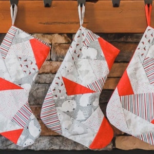 Może przedstawiać: Trzy czerwono-białe świąteczne skarpety z patchworkowym wzorem wiszące na kominku z cegły.