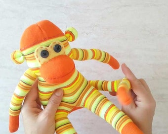 May include: A striped sock monkey toy with orange, yellow, and green stripes. The monkey has a bright orange face with black button eyes.