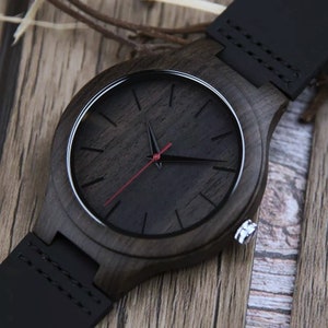 May include: A black wooden wristwatch with a black leather strap and a black face with red second hand.