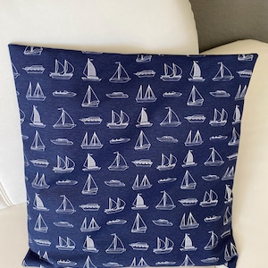 Könnte beinhalten: Marineblaues quadratisches Kissen mit einem sich wiederholenden Muster aus weißen Segelbooten. Das Kissen im maritimen Stil wird auf einer weißen Oberfläche präsentiert. Die Segelboote haben unterschiedliche Designs und verleihen dem Wohnaccessoire visuelles Interesse.