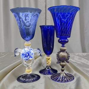 Peut inclure: Trois gobelets en verre bleu cobalt avec des pieds distincts. Le gobelet de gauche présente un motif floral gravé et une rose bleue. Le gobelet central est uni avec un pied doré. Le gobelet de droite a un pied texturé de couleur dorée.