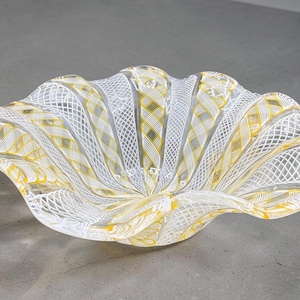 Peut inclure: Un bol décoratif en verre avec un bord festonné. Le bol présente une base transparente avec des motifs complexes blancs et jaunes. Le design comprend des motifs en losange et tissés, créant un aspect texturé. Le bol est probablement utilisé pour l'exposition ou le service.