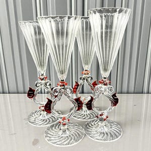 Peut inclure: Quatre flûtes à champagne transparentes avec un design côtelé. Les tiges présentent des accents de verre rouge et transparent et un motif tourbillonnant décoratif. Les flûtes ont une base ronde avec un motif en spirale.
