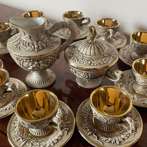 Puede incluir: Un juego de tazas de té y platillos de porcelana vintage con detalles dorados. El juego incluye una jarra de crema, un azucarero y seis tazas de té. Las tazas y los platillos presentan un diseño floral con ribetes dorados.