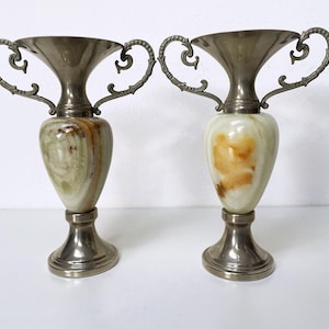Può includere: Due vasi in marmo verde e argento con manici decorati. I vasi sono su uno sfondo bianco.
