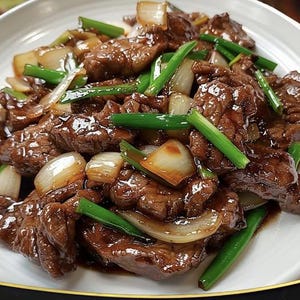 Puede incluir: Un plato de carne de res salteada con cebollas y cebolletas. La carne de res es de color marrón oscuro y parece estar cubierta con una salsa. Las cebollas son blancas y translúcidas, y las cebolletas son de color verde brillante.