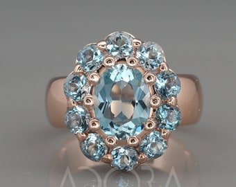 May include: A rose gold ring with a large oval-shaped blue topaz gemstone surrounded by a halo of smaller blue topaz gemstones.