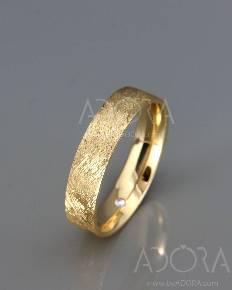 May include: A gold wedding band with a textured, brushed finish. The band is simple and has a subtle shine.