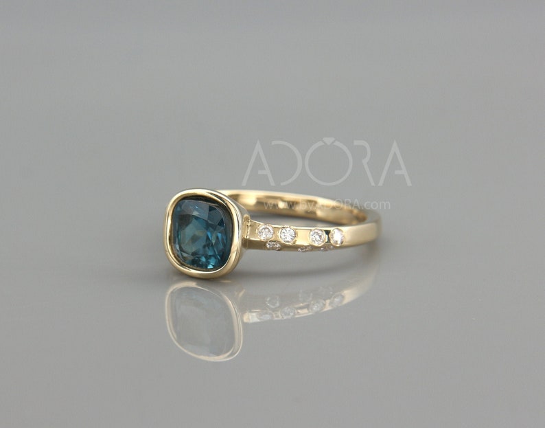 May include: A gold ring with a blue gemstone and small diamonds set in the band. The ring is on a gray background. ADORA.com