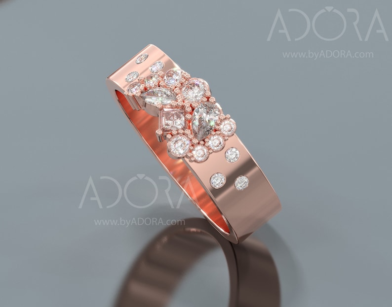 Pu&ograve; includere: Un anello con fascia in oro rosa con un gruppo di piccoli diamanti e un diamante pi&ugrave; grande a forma di pera al centro.