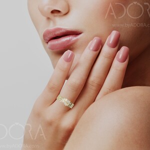 Pu&ograve; includere: Un anello a fascia d'oro con un gruppo di piccoli diamanti al centro. L'anello &egrave; sul dito di una donna.