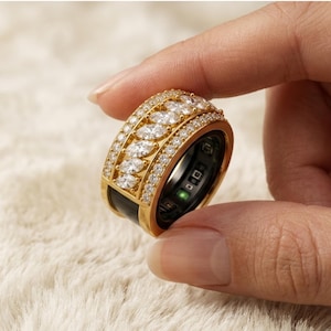 May include: A wide gold band ring featuring a central row of marquise-cut clear stones flanked by two rows of small round pavé-set stones. The interior of the ring is black with visible electronic sensor components and a small green light.
