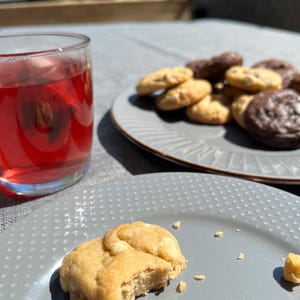 Puede incluir: Un vaso de l&iacute;quido rojo y un plato de galletas. Las galletas son una mezcla de chispas de chocolate y chocolate. Una galleta est&aacute; en un plato separado, con un bocado. Los platos son grises.
