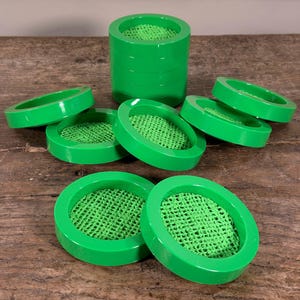 May include: Bright green, circular coasters with a mesh insert are arranged on a wooden surface. Some coasters are stacked, while others are scattered around. The coasters have a glossy finish and a modern design.