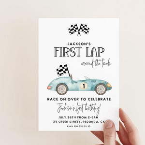 Puede incluir: Una invitación de cumpleaños de coche de carreras azul y blanco con una bandera a cuadros y el texto "Jackson's First Lap around the track". La invitación incluye la fecha, la hora y la ubicación de la fiesta.