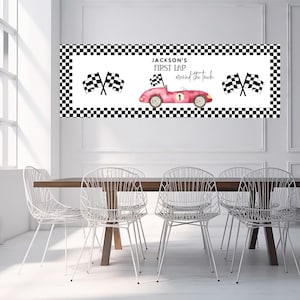 May include: A banner with a black and white checkered border and the text "Jackson's First Lap around the track". The banner features a pink race car, checkered flags, and the number 1.