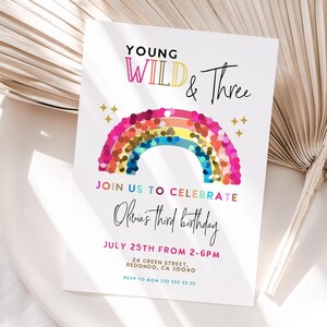 Könnte beinhalten: Weiße Einladungskarte mit dem Text "Young Wild & Three" und einem bunten Regenbogen-Design. Die Karte verkündet "Feiern Sie mit uns Olivias dritten Geburtstag" mit Datum, Uhrzeit und Adresse. Goldene Sterne sind ebenfalls abgebildet.